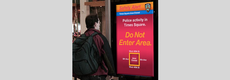 Picture of man looking at large screen reporting incident in times square.